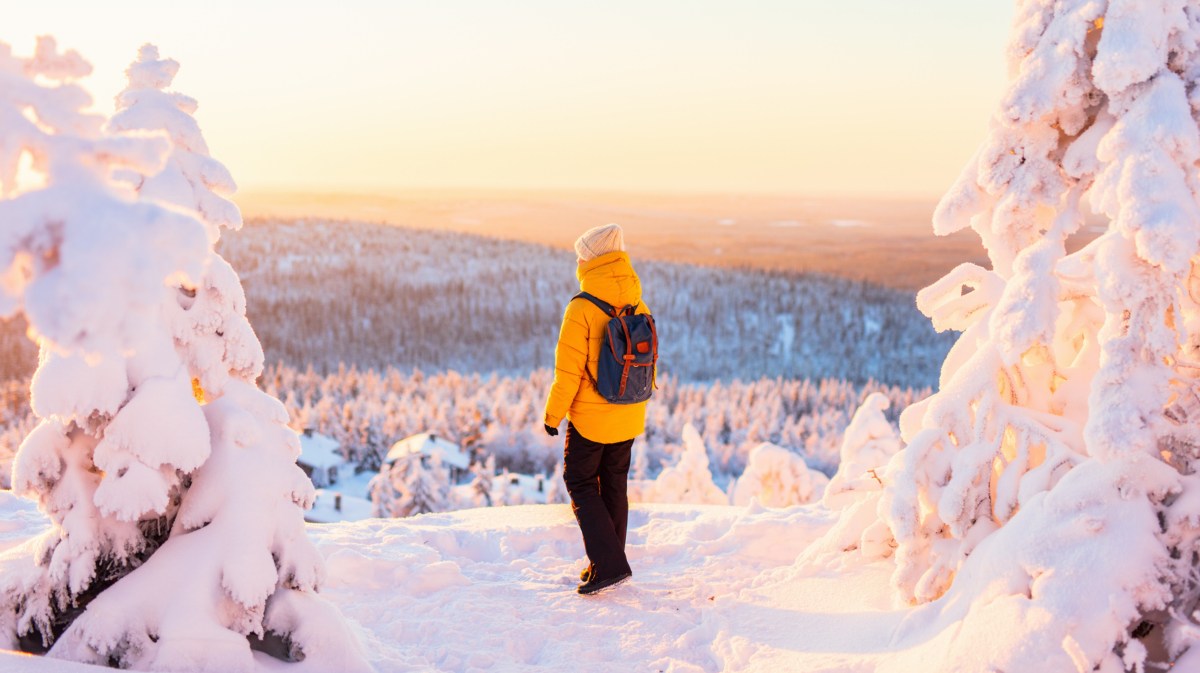 Person in gelber Winterjacke steht in verschneiter Landschaft