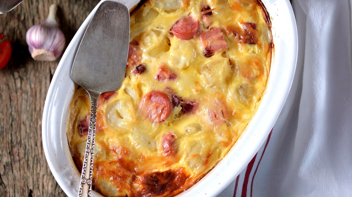 Kartoffelgratin mit Würstchen in weißer Auflaufform.