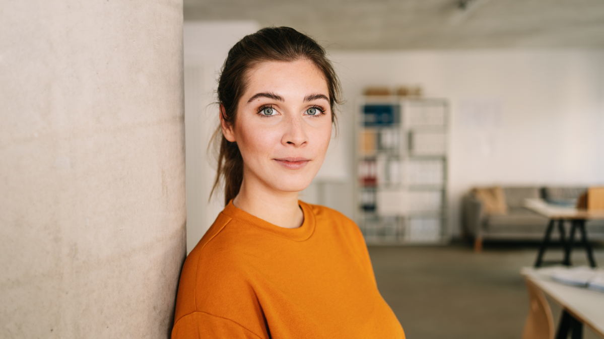 Frau mit orangenem Shirt, die seitlich in die Kamera blickt