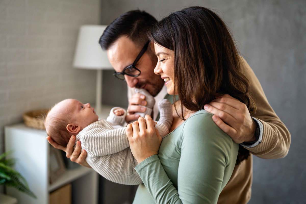 Mutter und Vater halten ihr Neugeborenes in den Armen und schauen es verträumt an.