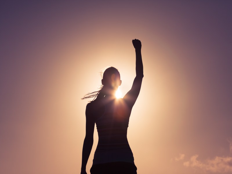 Silhouette einer Frau, die den Arm hebt, vor Sonnenlicht