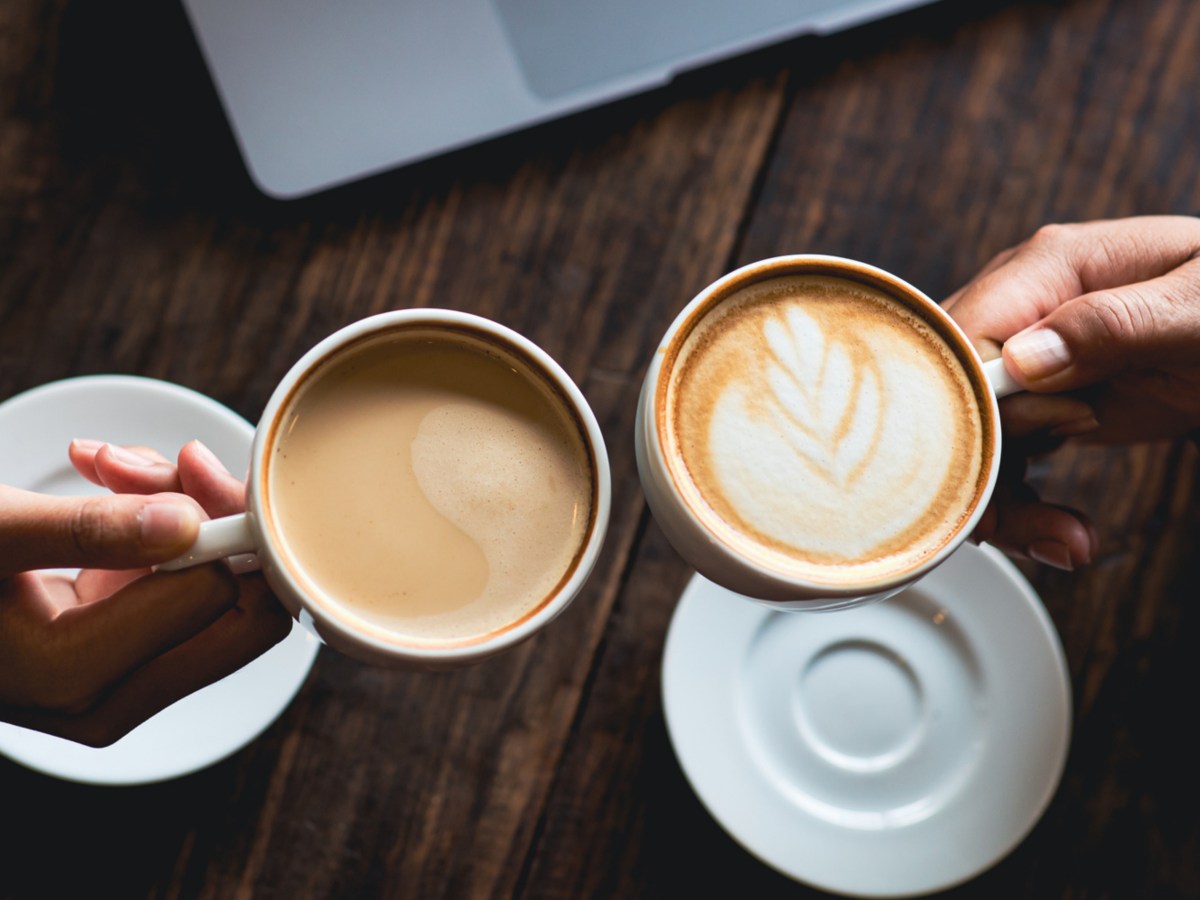 Zwei Frauen mit stoßen mit Kaffeetassen an.