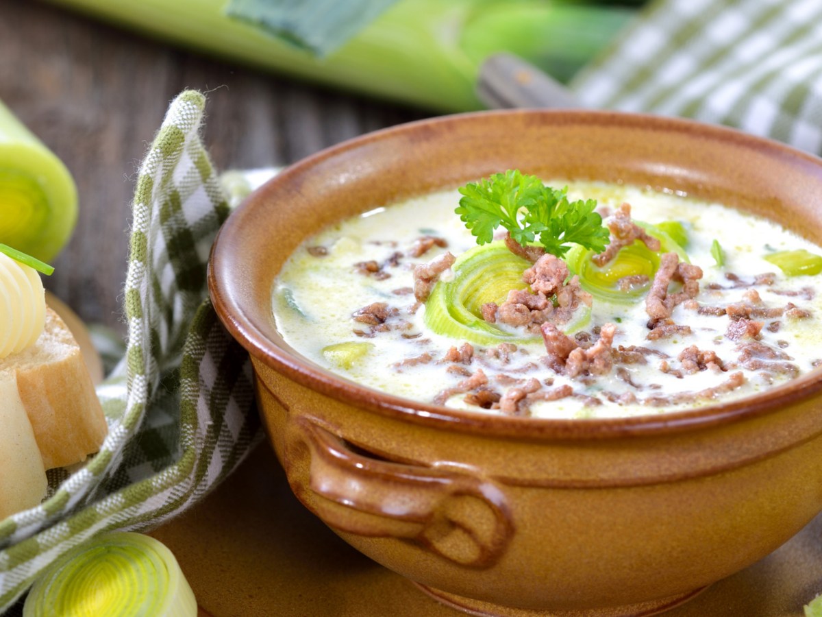 K&auml;se-Lauch-Suppe mit Hackfleisch in braunem Keramiktopf.