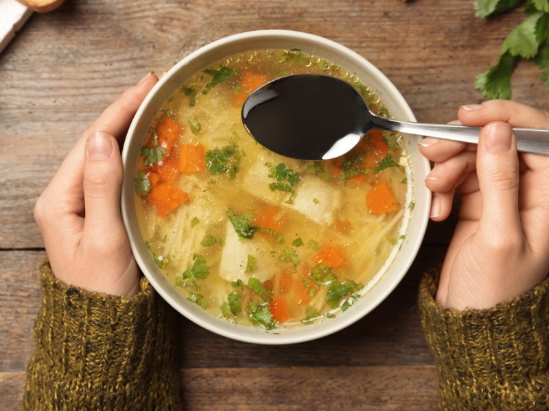 Schüssel Hühnersuppe mit Nudeln steht auf Holztisch.