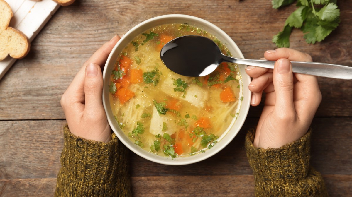 Schüssel Hühnersuppe mit Nudeln steht auf Holztisch.