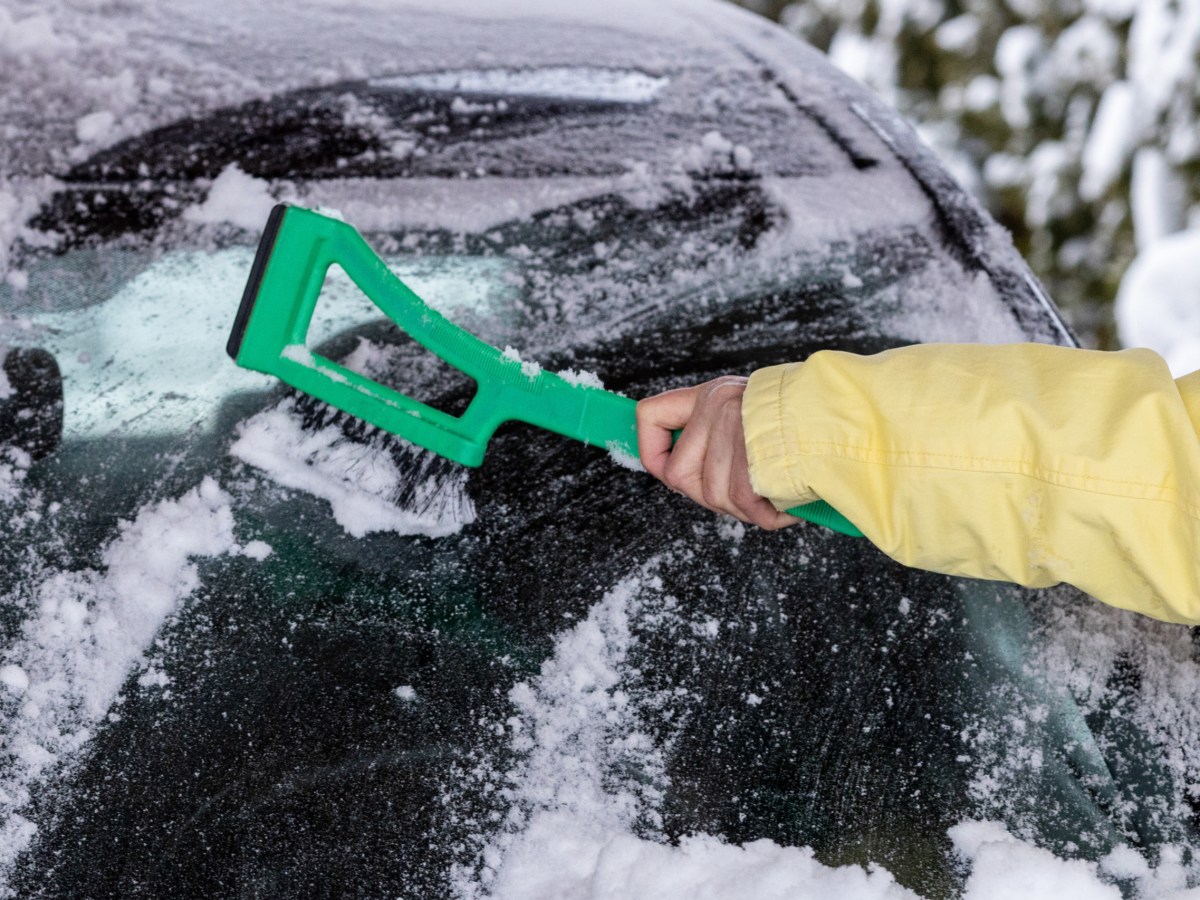 Eine Frau enteist die Frontscheibe ihres Autos mit einem Kratzwerkzeug.
