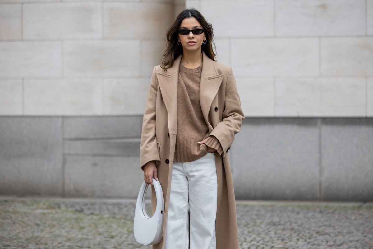 Influencerin, die zur weißen Jeans einen beigen Mantel und Pullover kombiniert