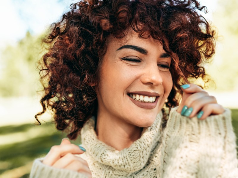 Frau mit Locken und blauem Nagellack, die sich lächelnd zur Seite dreht