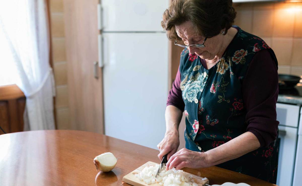 Omas Hausmittel gegen Husten: Ältere Frau schneidet Zwiebel auf Brett