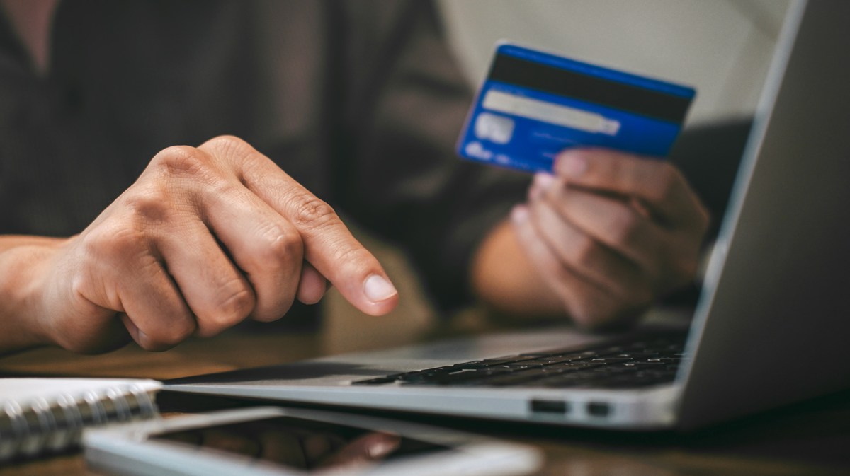 Frau hält Bankkarte in der Hand und tippt auf dem Laptop.