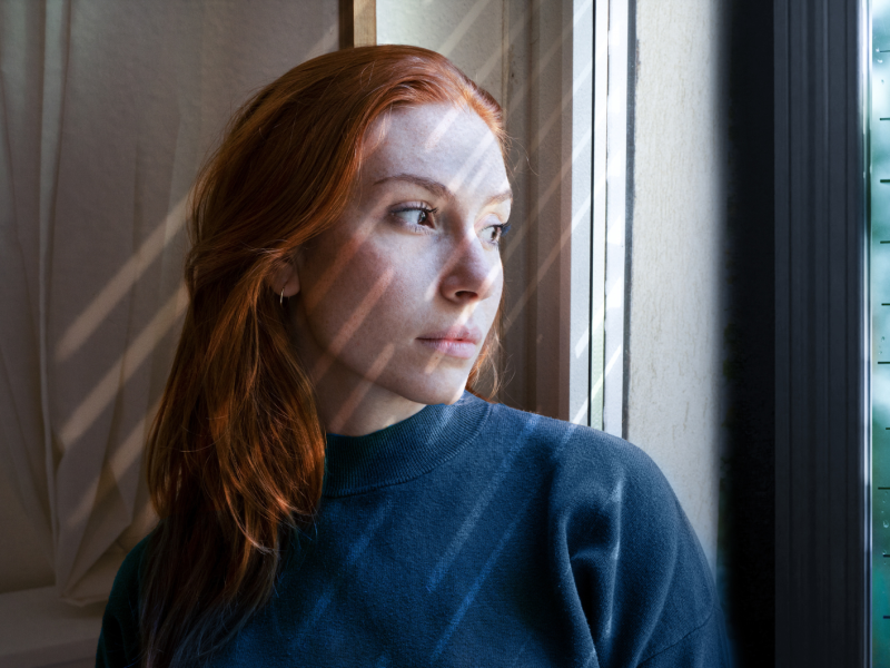 Rothaarige Frau, die nachdenklich aus dem Fenster schaut