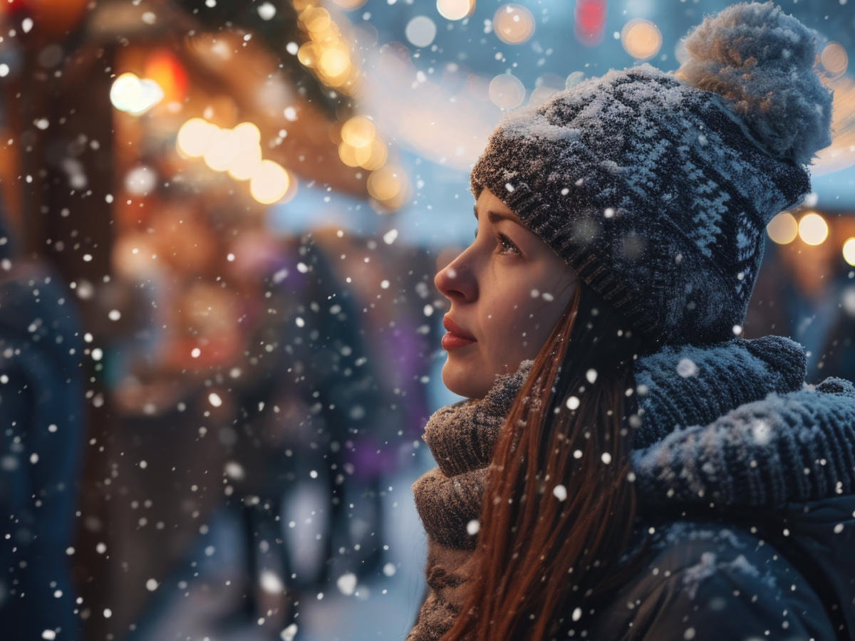 Frau im Schnee vor einer Hütte, die nachdenklich ins Leere starrt