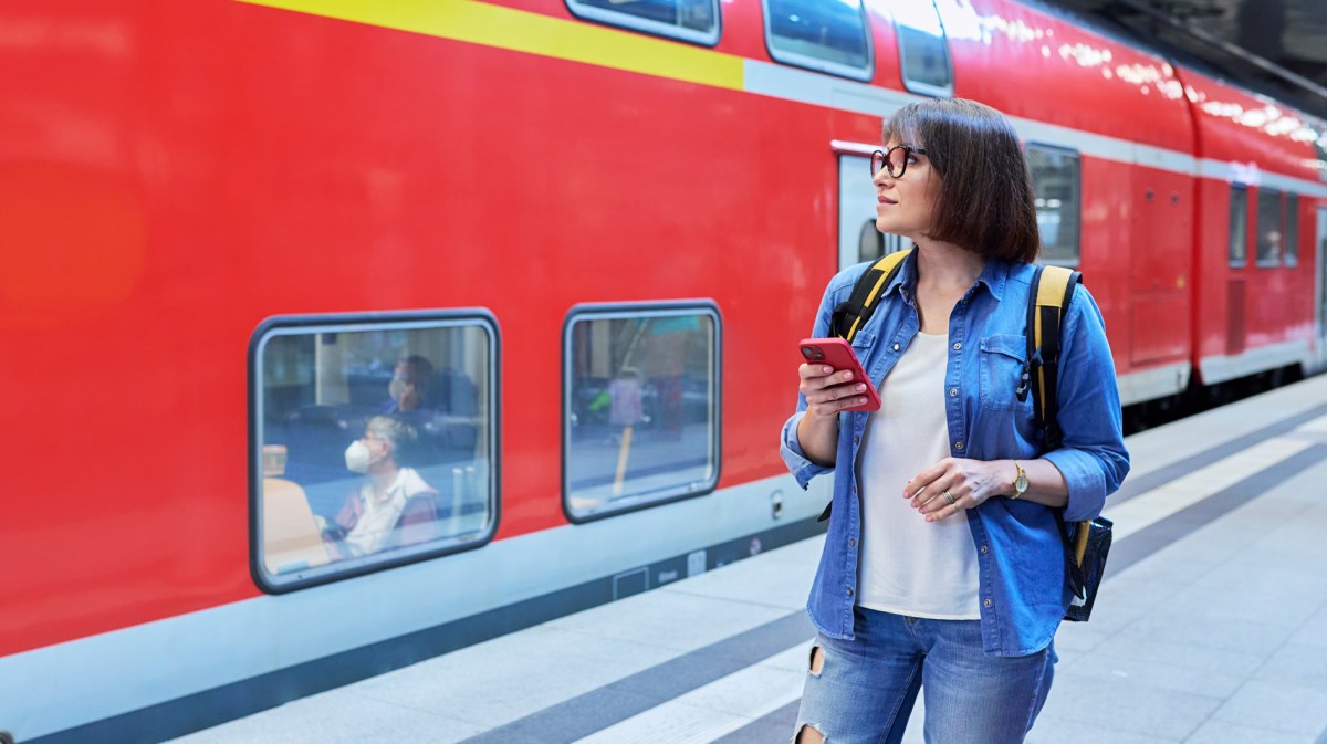 Frau steht mit dem Handy am Bahnsteig.