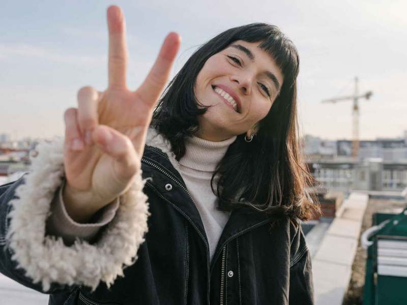 Junge Frau mit braunen Haaren zeigt das Peace Zeichen.