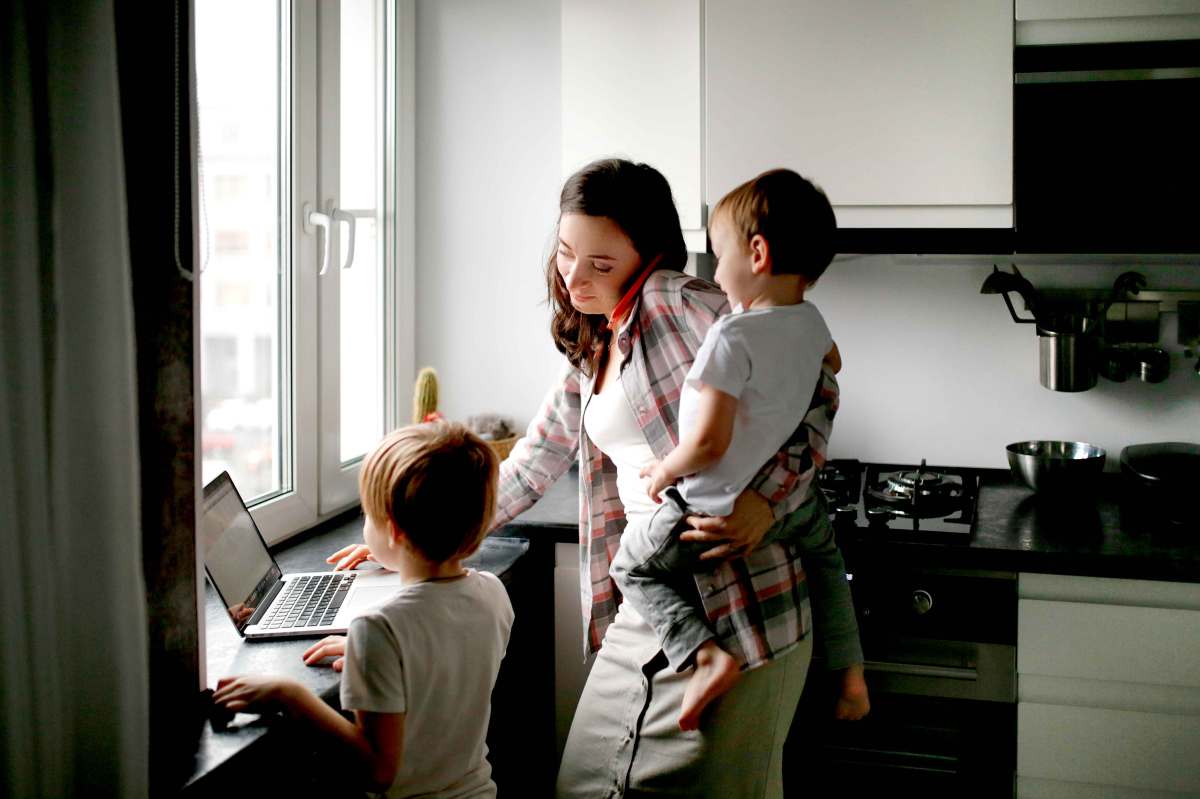 Beschäftigte Mutter von zwei Jungs arbeitet am Laptop.