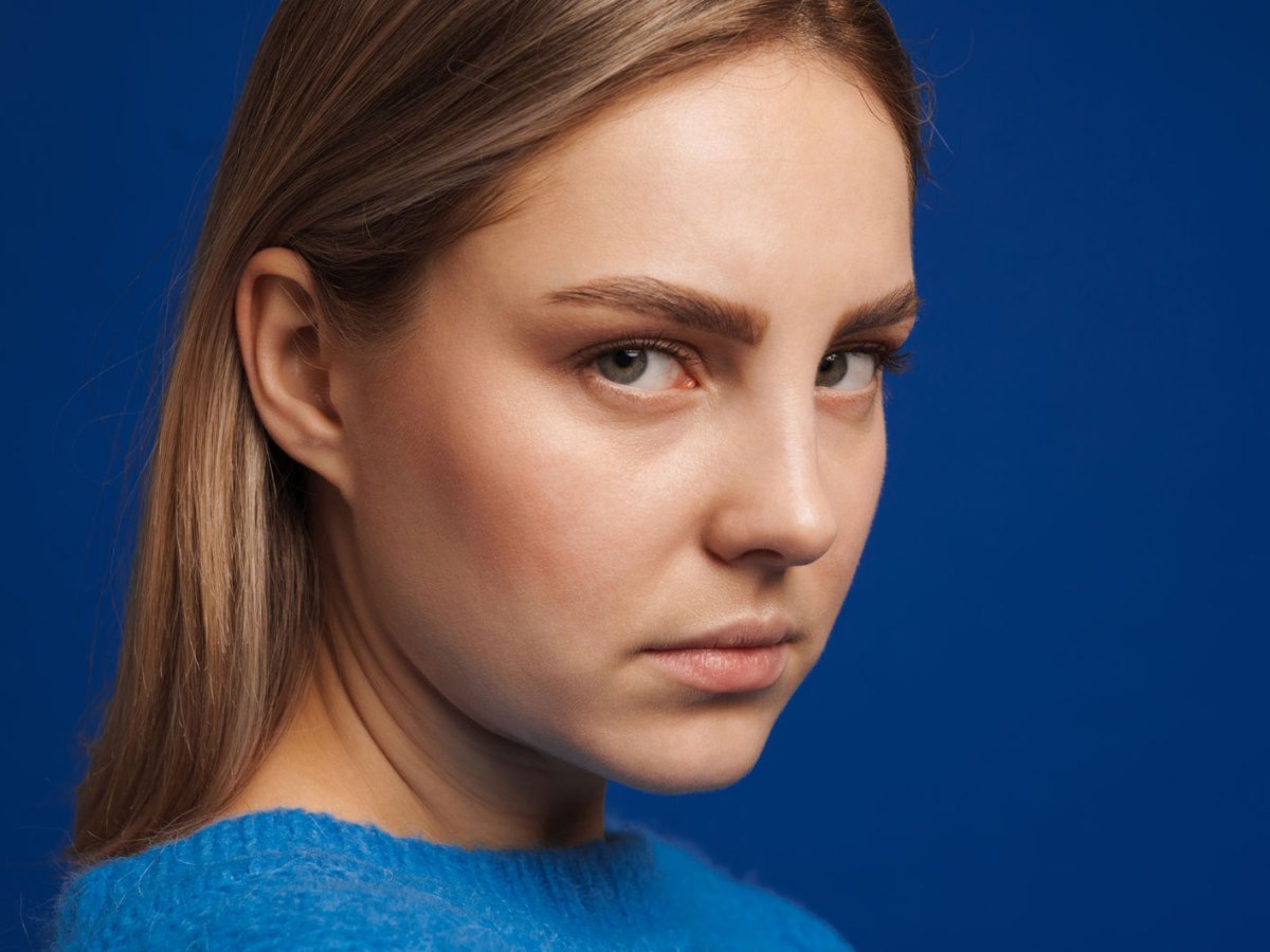 Blonde Frau schaut ernst in die kamera, dahinter blauer Hintergrund