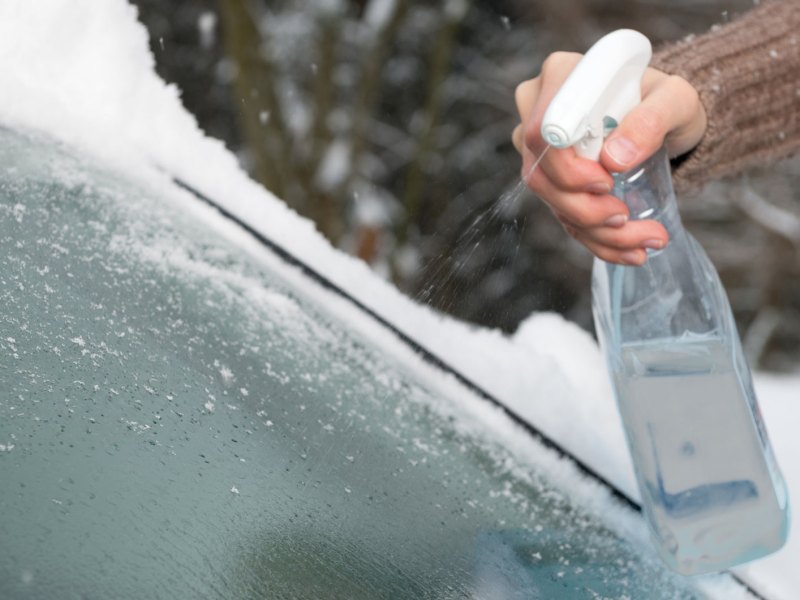 Person enteist die Scheibe mit Sprayflasche