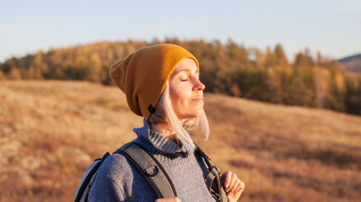 Frau in der Natur, die genussvoll in die Sonne blickt und einatmet