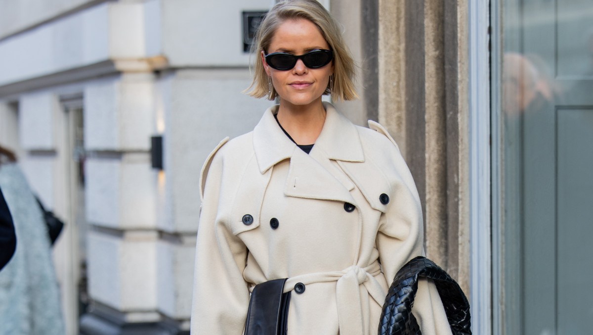 Cathrine Leth Damgaard wears beige trench coat, black bag, gloves, skirt, sunglasses outside The Garment during the Copenhagen Fashion Week AW24 on January 31, 2024 in Copenhagen