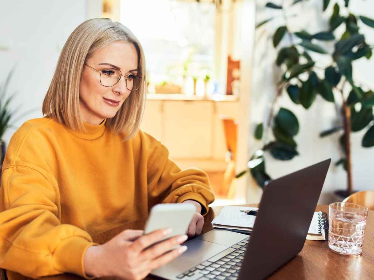 Frau mit gelben Pullover sitzt am Schreibtisch vor ihrem Laptop.