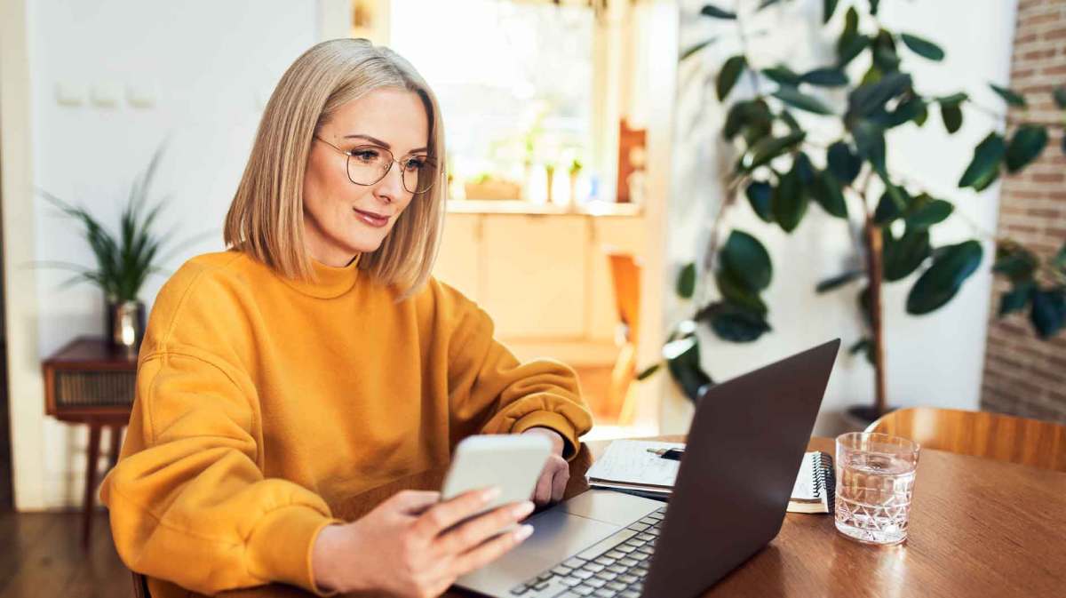 Frau mit gelben Pullover sitzt am Schreibtisch vor ihrem Laptop.