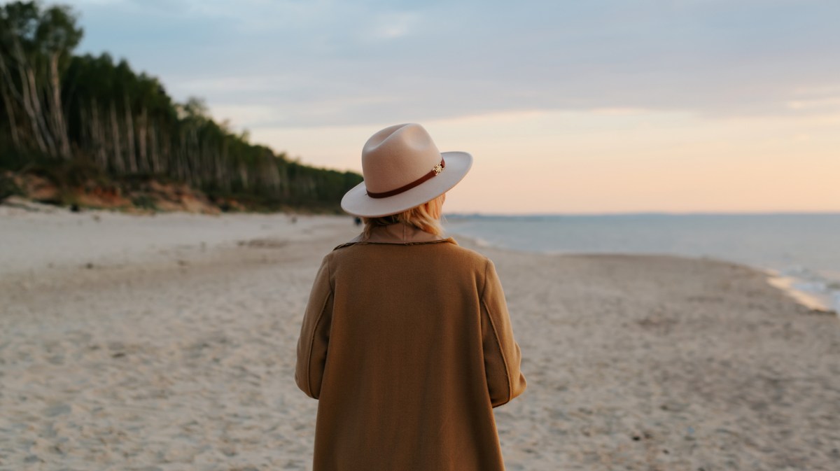 Frau mit Hut am Strand, die in den Sonnenuntergang läuft