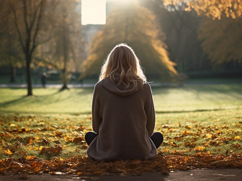 Frau im Park, die im Schneidersitz auf dem Rasen sitzt