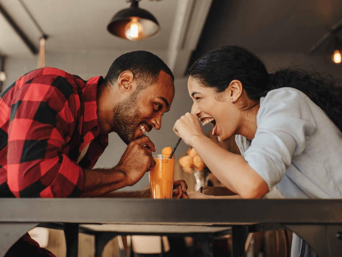 Frau und Mann in einem Caf&eacute;, die sich anlachen und dabei ein Getr&auml;nk trinken.