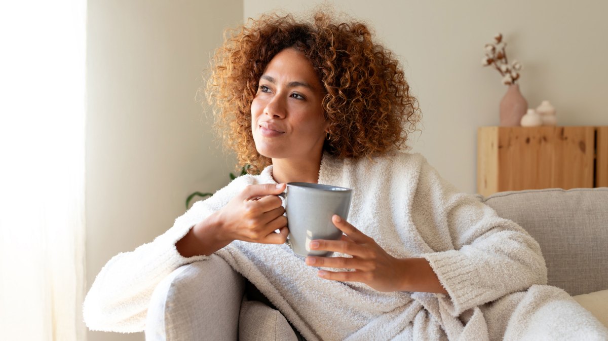 Frau sitzt auf dem Sofa und hält eine Tasse Kaffee in der Hand