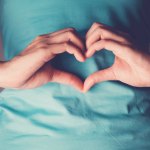 Frau macht mit ihren H&auml;nden ein Herzzeichen vor ihrem Bauch