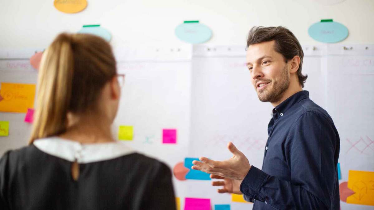 Mann erklärt einer Frau etwas vor einem Flipchart.