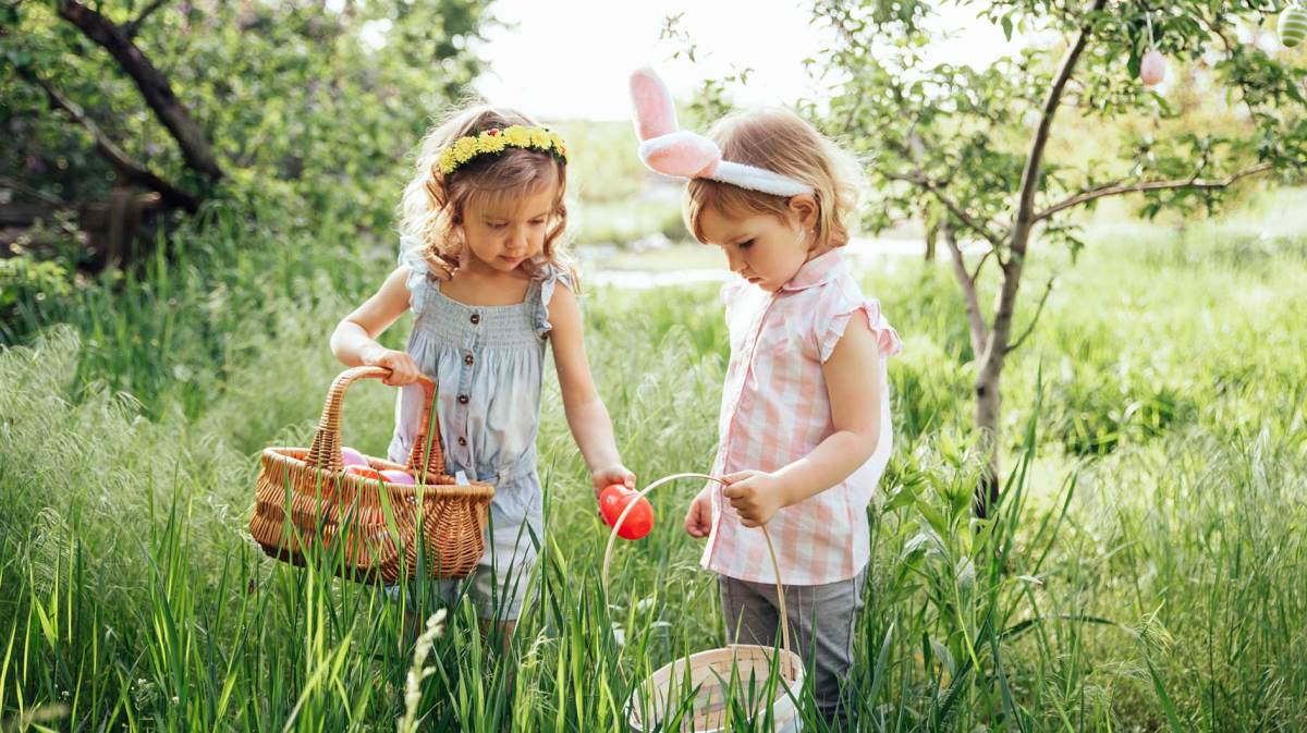 Zwei kleine Mädchen suchen nach Ostereiern auf einer großen Wiese.