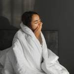 Eine m&uuml;de Frau hat nicht genug Schlaf bekommen. Schlaflosigkeit in der Nacht und psychische Gesundheit. Sch&ouml;nes Morgenlicht im Schlafzimmer.