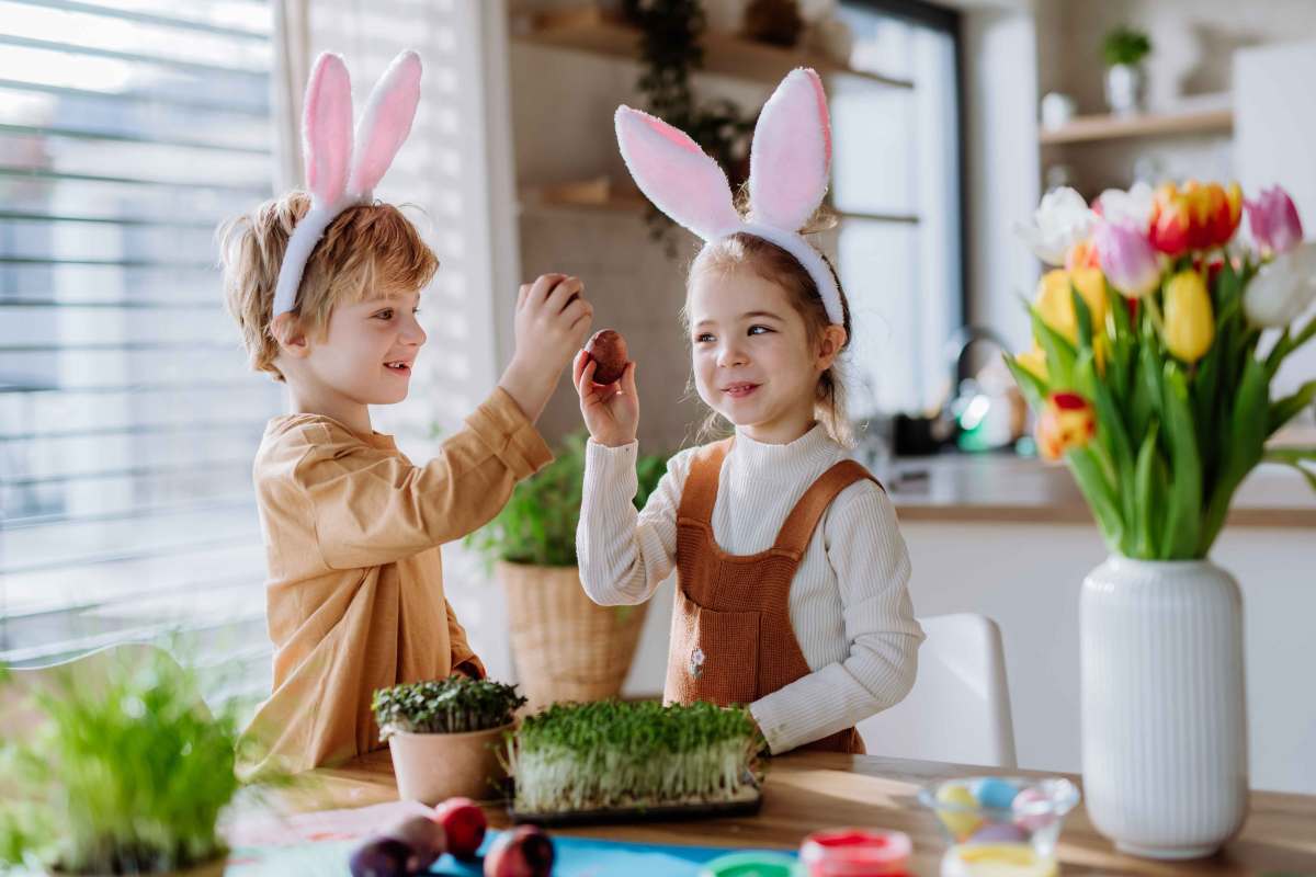 Kleine Kinder mit Hasenohren feiern Ostern und spielen ein Osterspiel mit Eiern.