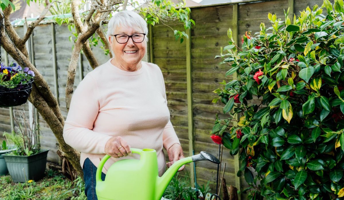 Ältere Frau im Garten mit grüner Gießkanne