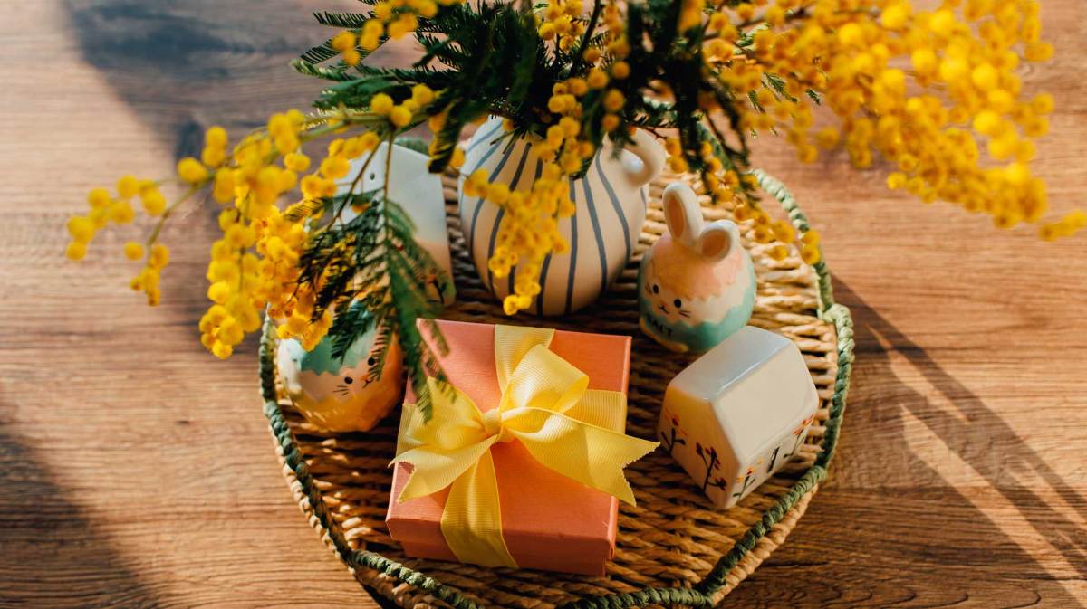 Geschenk, das auf einem Osterkorb steht, neben einem Porzellanhasen und einem kleinen Blumenstrauß.