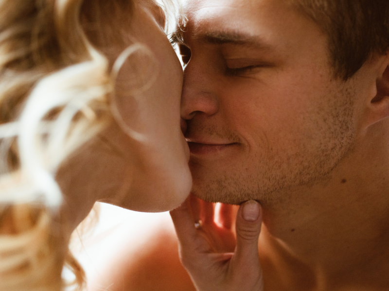 Ein junges Paar in Nahaufnahme berührt sich zärtlich, die blonde Frau hält das Kinn des lächelnden Mannes.