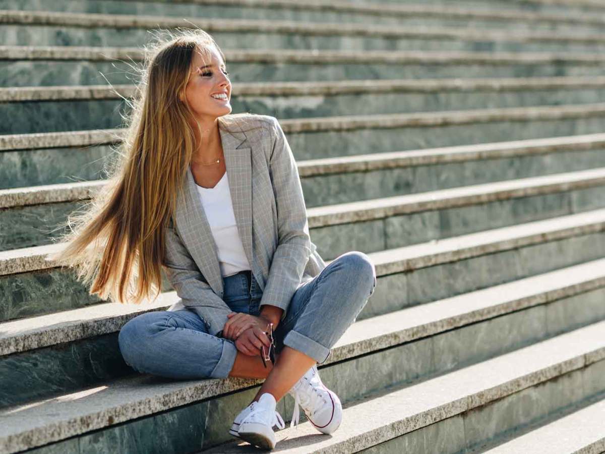 Frau mit langen Haaren sitzt drau&szlig;en auf einer Treppe im Fr&uuml;hling und lacht.