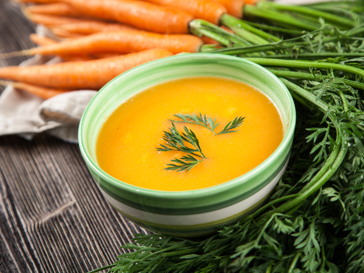 Cremige Karottensuppe in grüner Schale im Hintergrund frische Karotten.