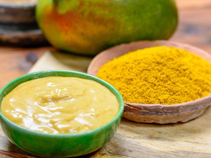 Gelber Curry-Dip in einer grünen, kleinen Schale, dahinter eine Schale mit Currypulver.