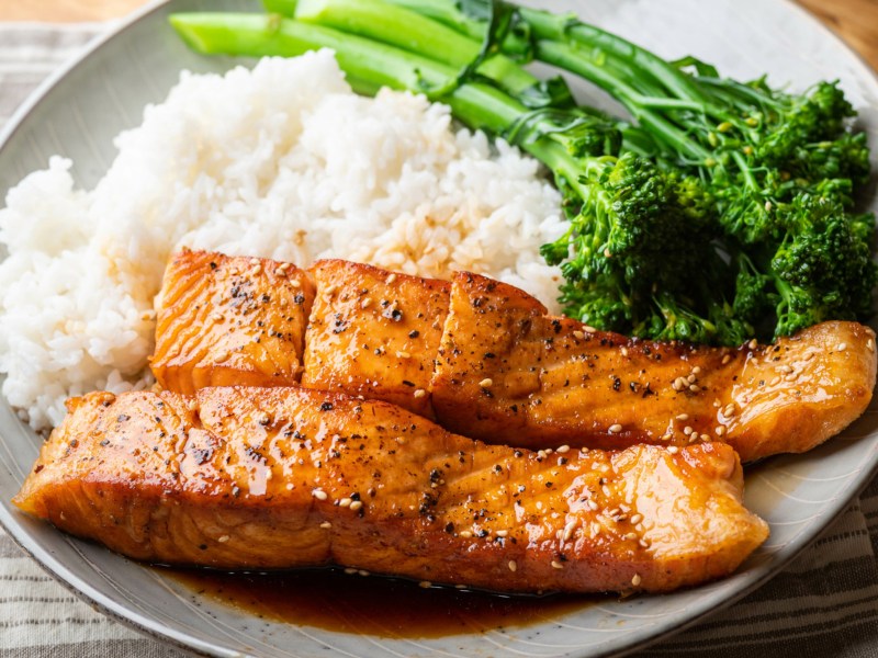 Teriyaki-Lachs mit weißem Reis und Brokkolini auf beigem Teller.