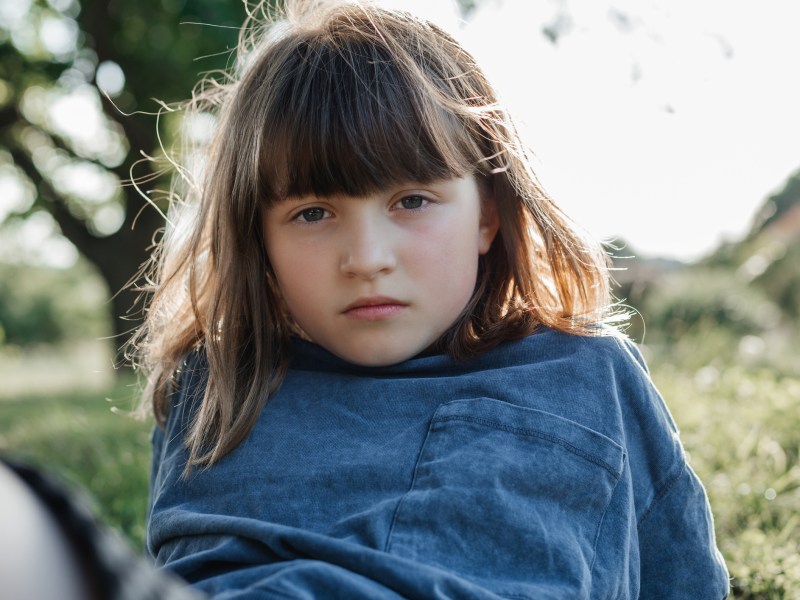 braunhaariges Mädchen schaut ernst in die kamera. Sie trägt ein blaues Oberteil