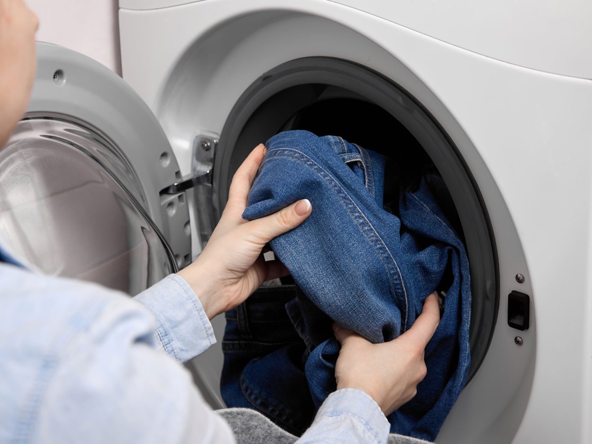 Frau, die eine Waschmaschine mit Jeanshosen bef&uuml;llt