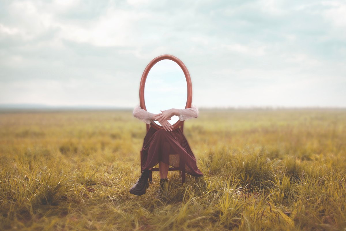 Frau sitzt mit einem Spiegel auf dem Schoß auf einer Wiese