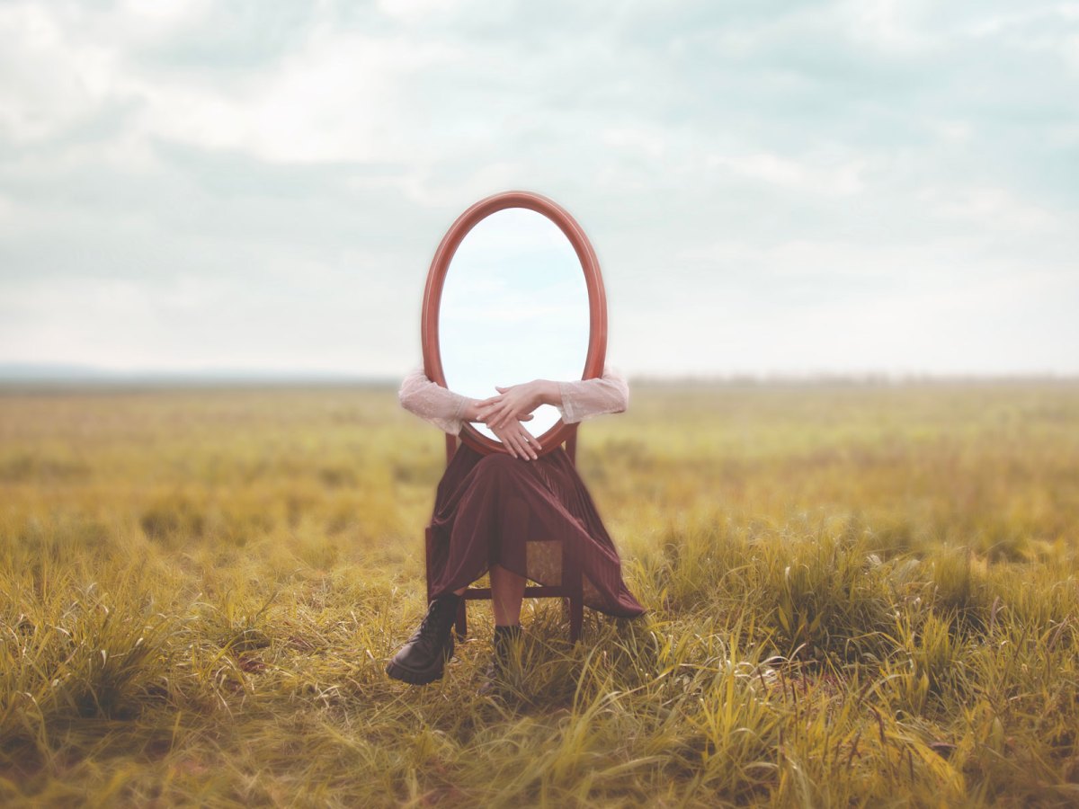 Frau sitzt mit einem Spiegel auf dem Schoß auf einer Wiese