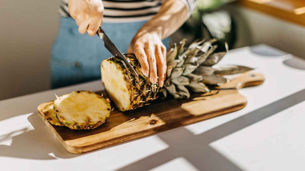 Frau schneidet eine Ananas auf einem Brett.