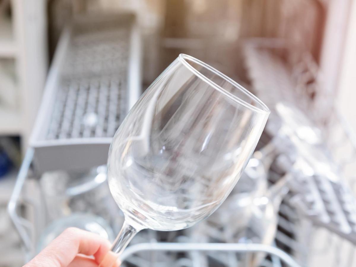 Frau holt ein milchiges Weinglas aus der Spülmaschine.