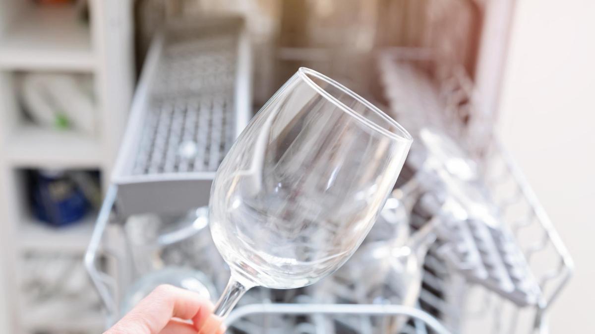 Frau holt ein milchiges Weinglas aus der Spülmaschine.