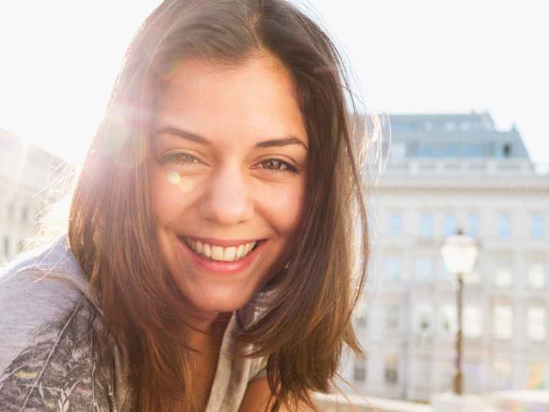 Frau mit braunem Longbob lächelt und wird von der Sonne angestrahlt.
