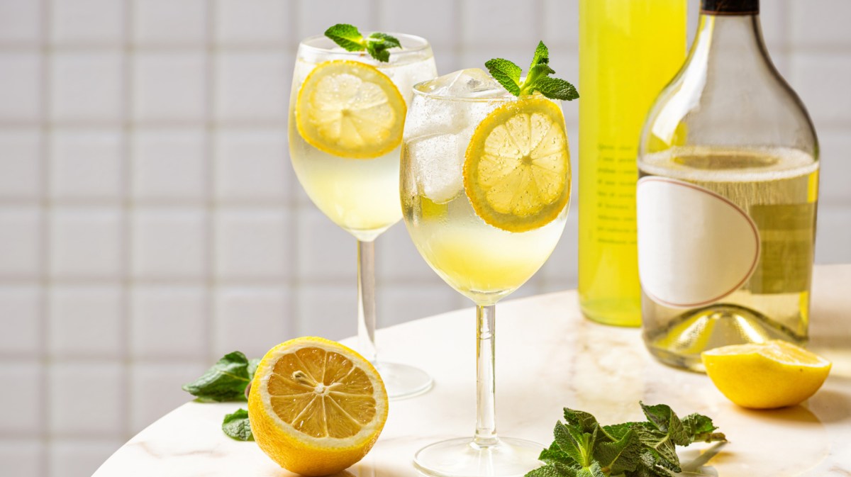 Zwei Gläser mit Limoncello Spritz auf einem weißen Tisch, eine halb aufgeschnittene Zitrone daneben.